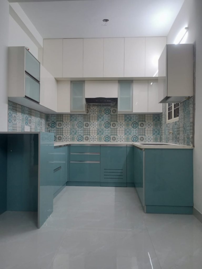Chic and airy modular kitchen interior by Galaxy Interior Designers, featuring a refreshing palette with teal cabinetry and decorative patterned tiles