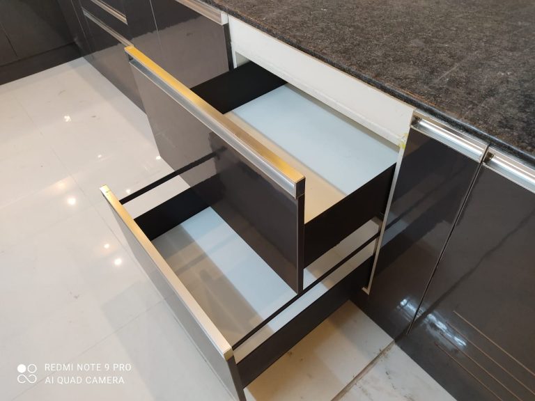 Customized modular kitchen drawer design by Galaxy Interior Designers in Chennai, featuring sleek black and white finishes with modern chrome handles