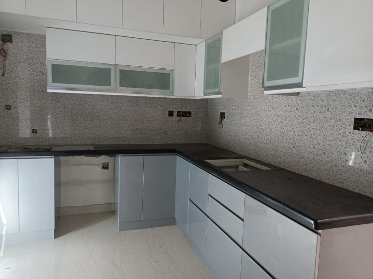 Under-construction view of a sophisticated modular kitchen interior by Galaxy Interior Designers, with elegant grey cabinetry and a patterned backsplash
