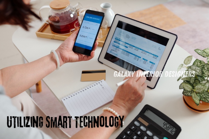 A person using smart technology for online banking and financial management at home, integrating multiple devices such as a smartphone, tablet, and calculator. Galaxy Interior Designers in Chennai promotes the use of advanced technology to enhance modern living spaces